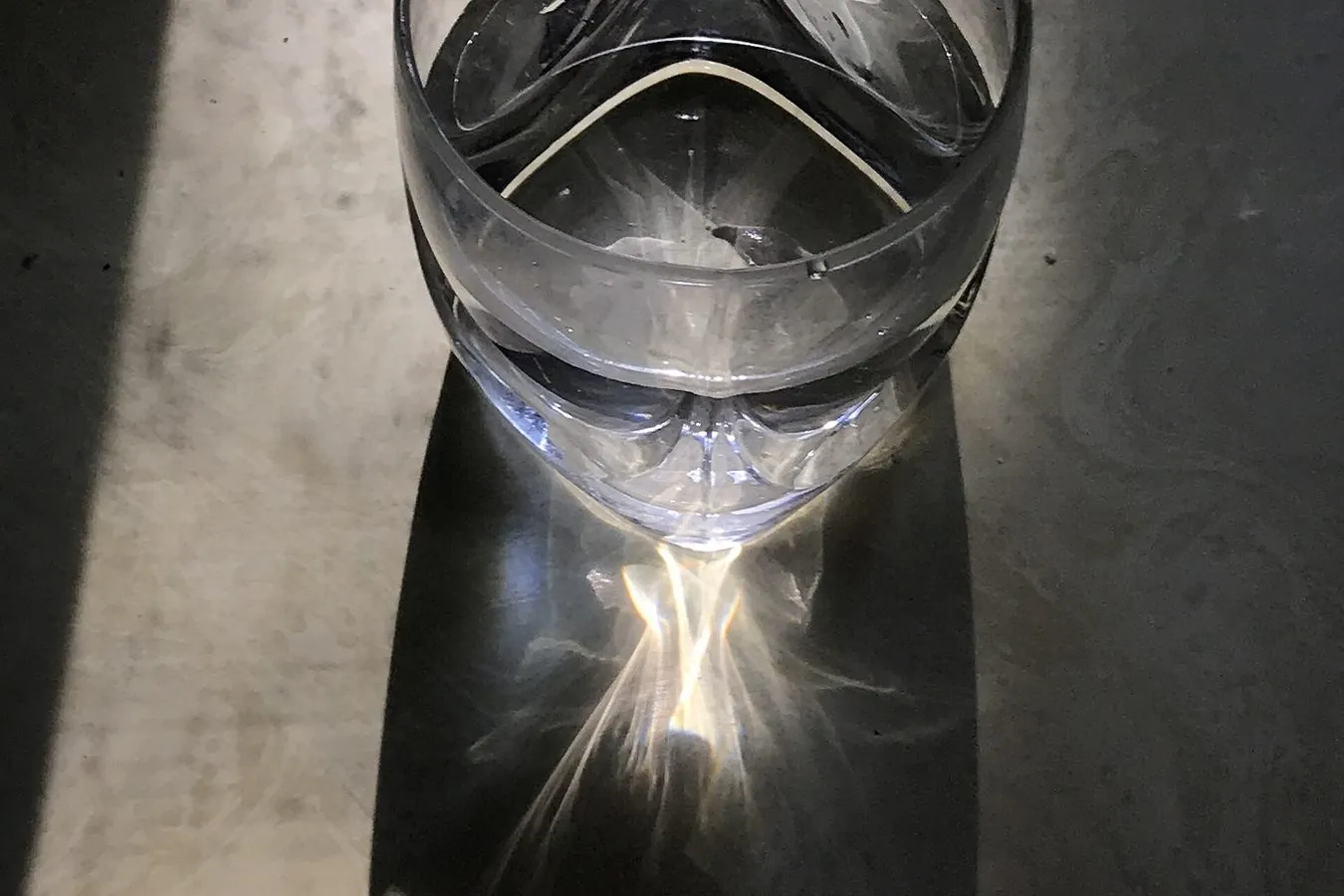 A glass of water in late-afternoon window light, casting a bright reflection onto the surface below