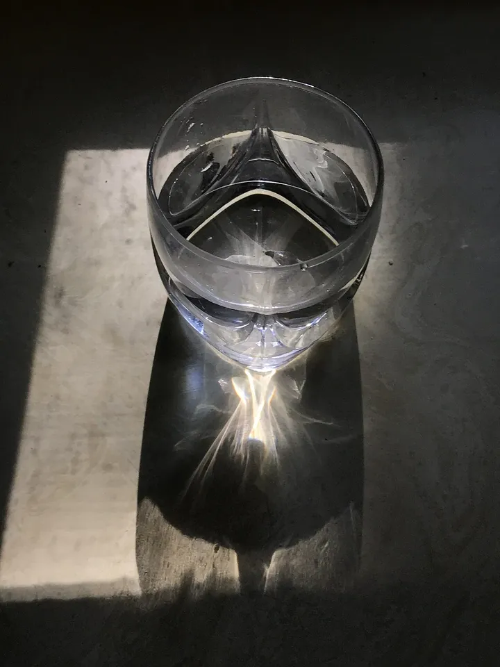 A glass of water in late-afternoon window light, casting a bright reflection onto the surface below