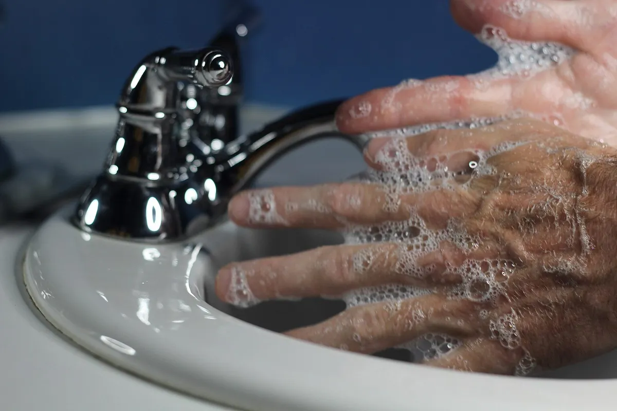 Soapy hands being rubbed together over a white sink beside a chrome tap