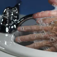 Soapy hands being rubbed together over a white sink beside a chrome tap.