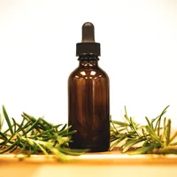 An amber glass dropper bottle standing between sprigs of fresh rosemary on a warm wooden surface.
