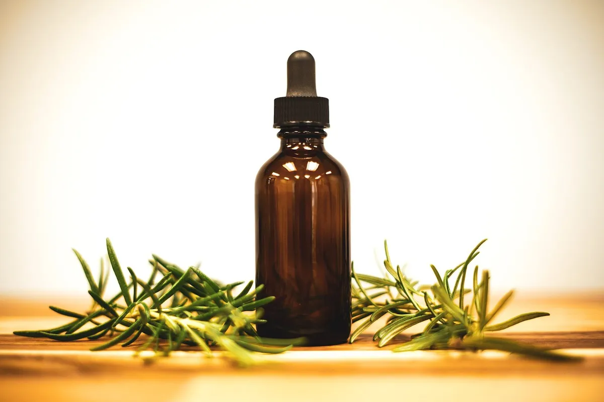 An amber glass dropper bottle standing between sprigs of fresh rosemary on a warm wooden surface.