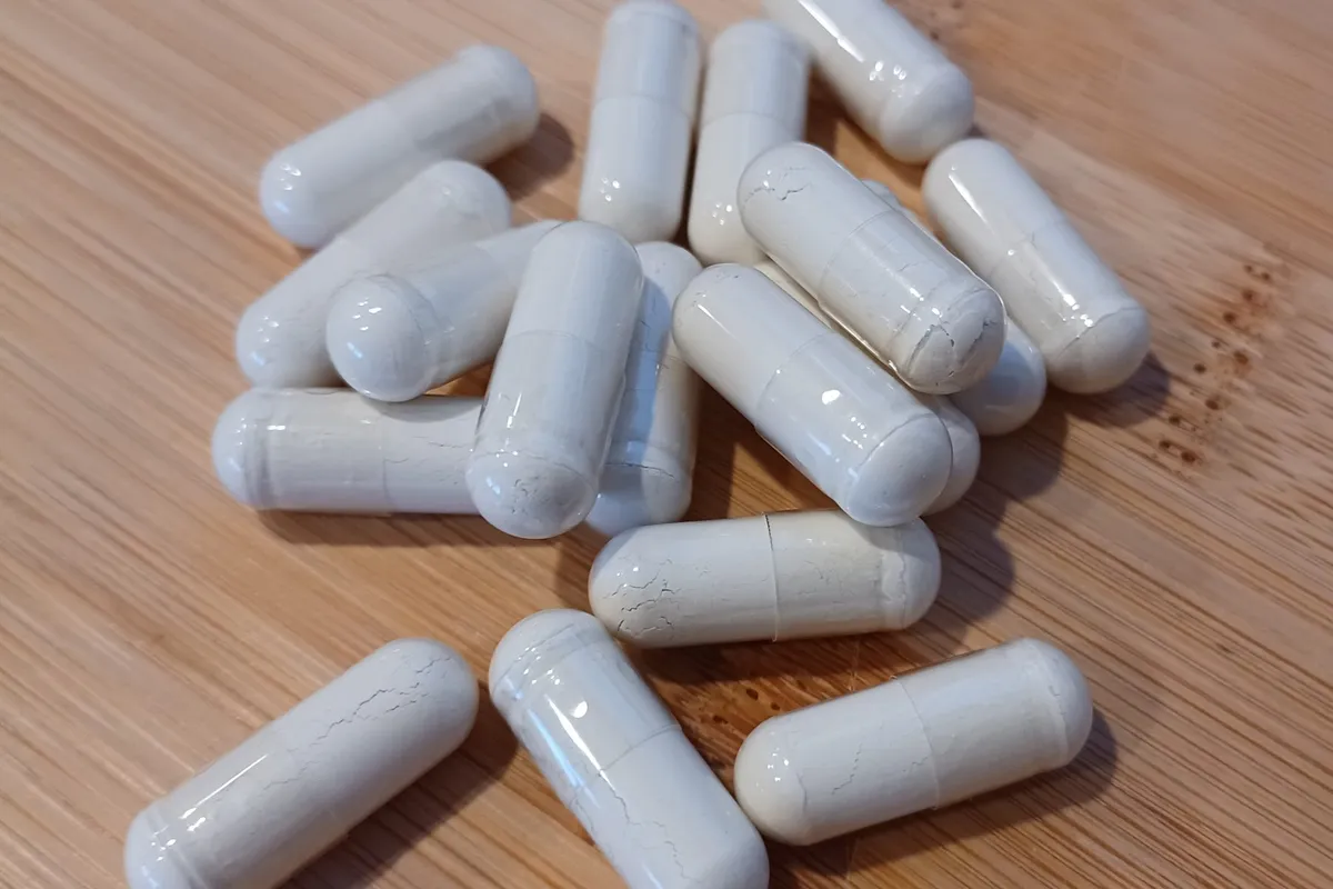 A loose scatter of plain white capsules on a pale wooden tabletop.