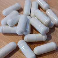 A loose scatter of plain white capsules on a pale wooden tabletop.