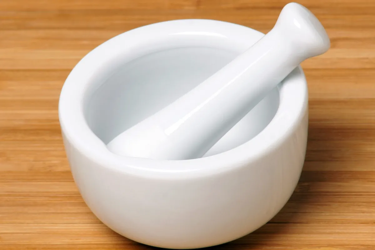 A small white porcelain mortar and pestle on a bamboo surface.