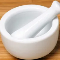 A small white porcelain mortar and pestle on a bamboo surface.