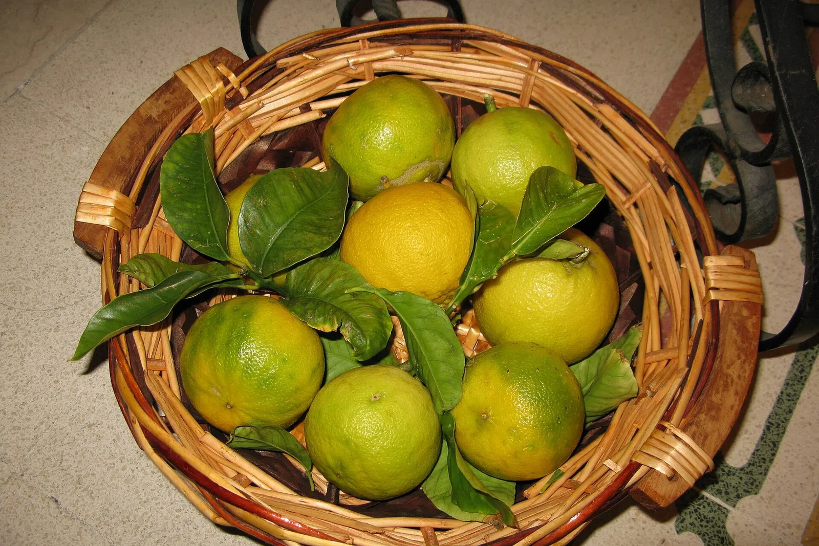 A woven basket filled with green and yellow bergamot fruits and a few of their leaves.