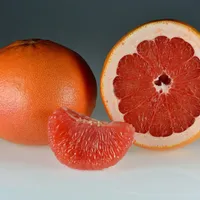 A whole red grapefruit beside a halved one and a single peeled segment on a pale background.