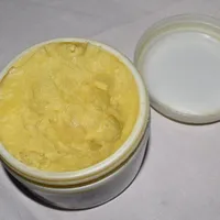 An open tub of whipped shea butter blended with essential oils, its lid set beside it on a pale cloth.