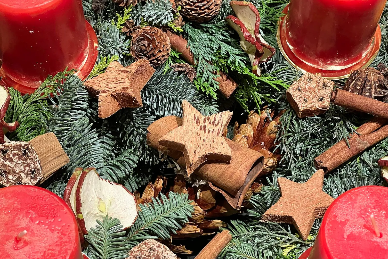 Fir sprigs, pine cones, cinnamon sticks, star anise and dried apple slices arranged between plain red candles on an Advent wreath.