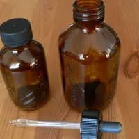 Two small amber glass bottles and a glass dropper with a black bulb on a pine table.