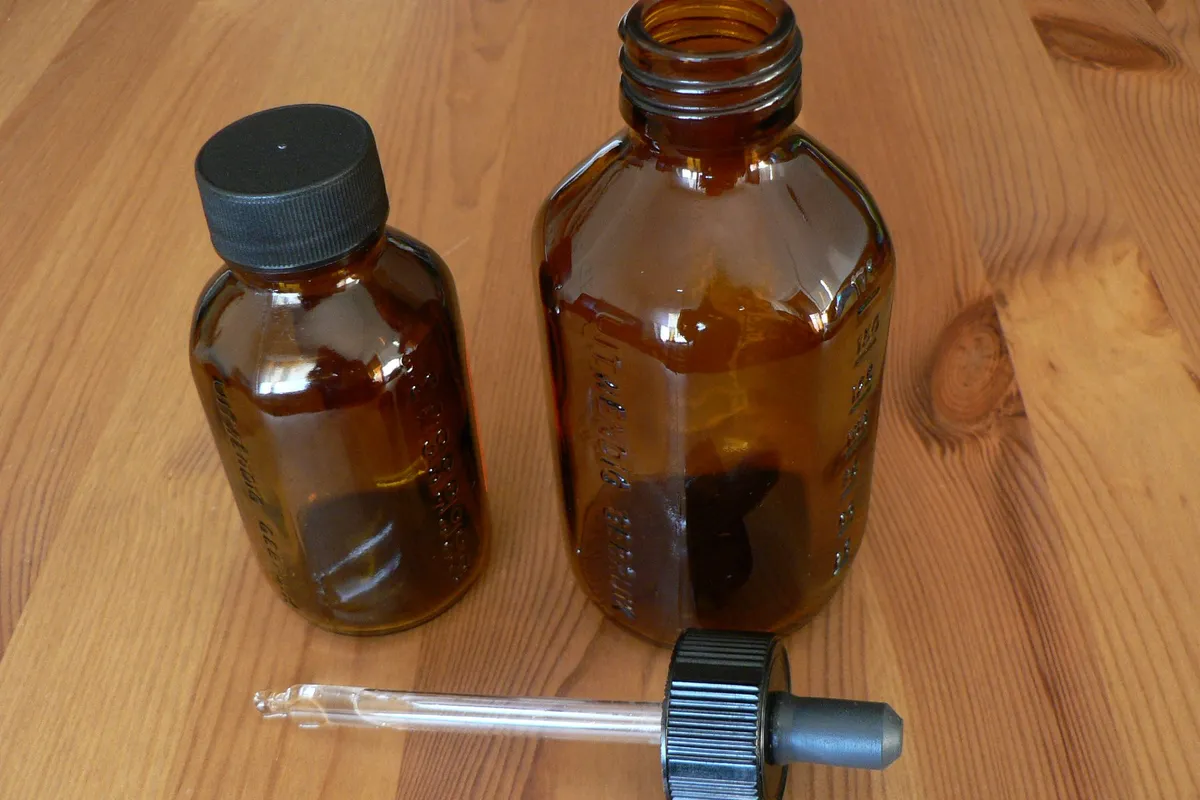 Two small amber glass bottles and a glass dropper with a black bulb on a pine table