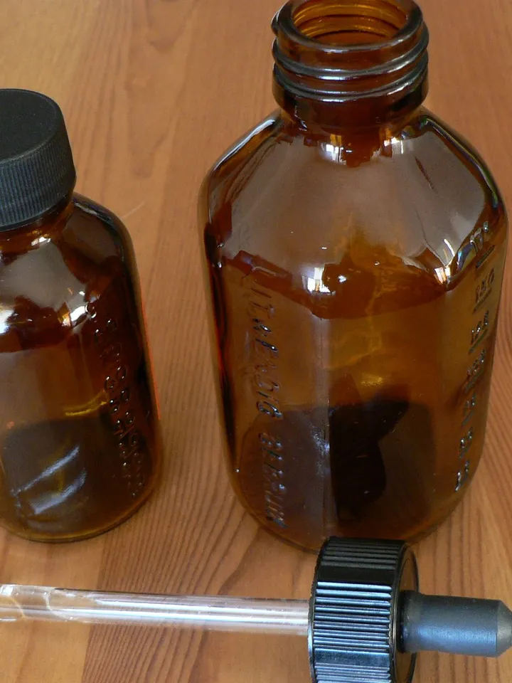 Two small amber glass bottles and a glass dropper with a black bulb on a pine table